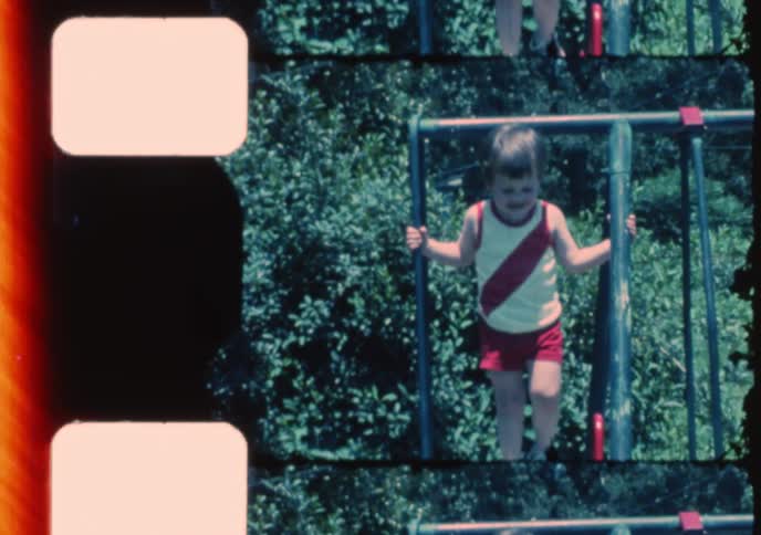 Vintage split-screen film of two young brothers happily playing on a slide and swing set in their backyard on a sunny day