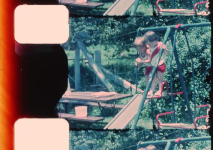 A charming vintage home movie shows two young children playing together on a backyard swing set and sliding into a wading pool on a sunny day