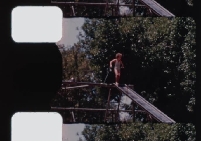A nostalgic home movie from the 1960s captures the joy of young children playing on a large metal slide at a sunny park