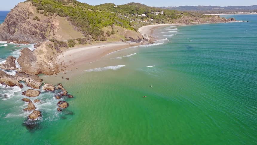An epic aerial reveal of the turquoise ocean and sandy beach leading to the iconic Cape Byron Lighthouse in Australia