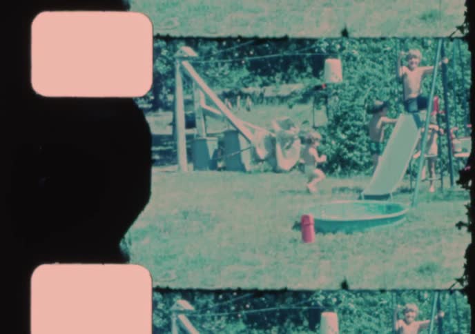 Vintage 8mm home movie footage shows a group of children playing on a swing set and slide in a backyard during the summertime