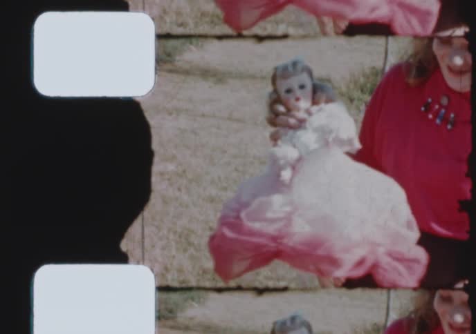 A scanned 8mm film strip shows a smiling young boy and his sister proudly holding her new doll in the 1950s