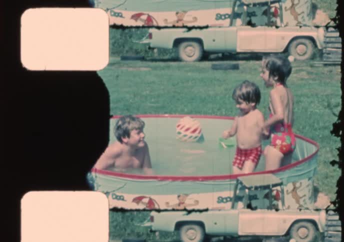 Vintage 8mm footage shows three young children splashing and playing happily in a Scooby Doo themed kiddie pool in their backyard on a sunny day
