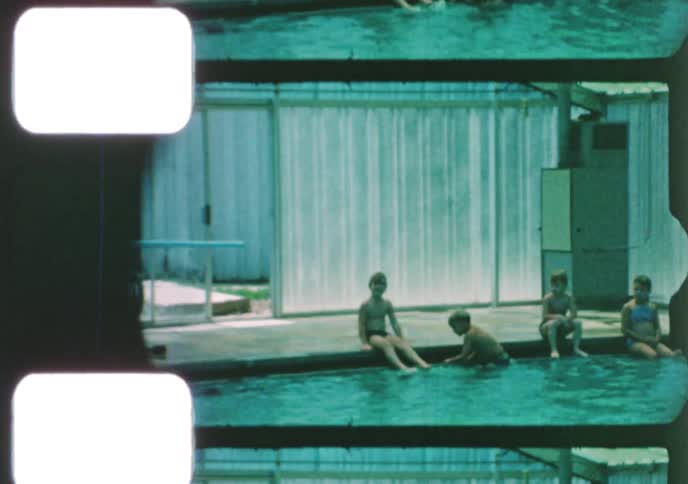 Retro 8mm home movie footage shows families and children swimming and playing at an indoor public pool