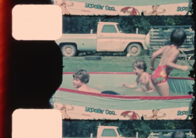 Vintage 8mm home movie captures the carefree joy of three young children splashing and playing in a backyard kiddie pool on a sunny summer day