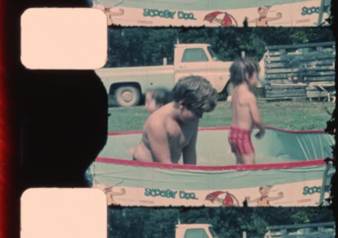 Archival film of children laughing and splashing in a backyard Scooby-Doo wading pool on a sunny day