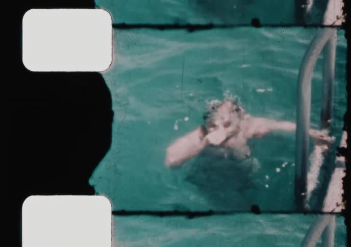A smiling young girl enjoys a sunny day swimming in a pool, captured on vintage 8mm film