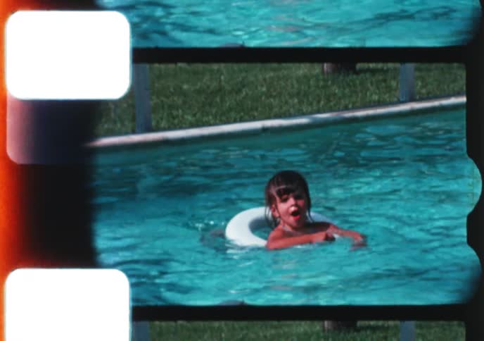 Authentic vintage home movie captures two young children happily playing and swimming in their backyard pool