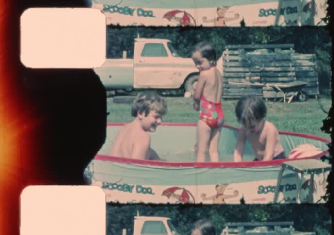 Authentic vintage home movie footage shows a group of happy children splashing and playing in a small backyard wading pool on a sunny summer day