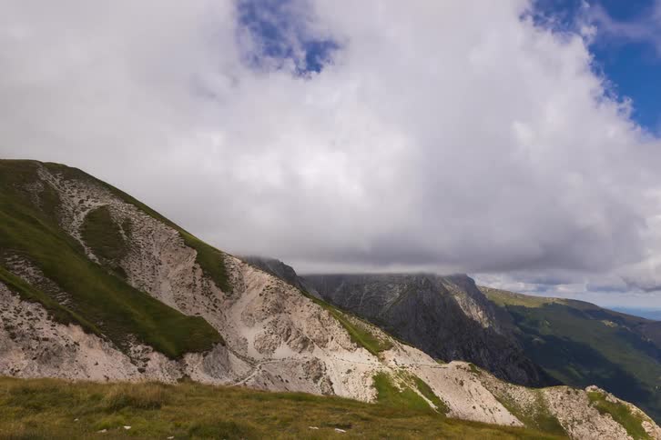 A timelapse of dramatic storm clouds moving quickly over a rugged green and rocky mountain landscape
