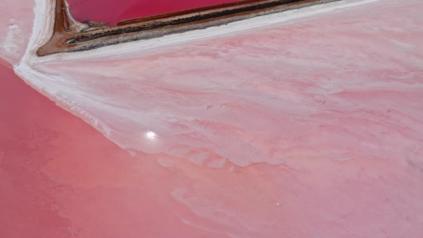 An aerial shot slowly pulls back to reveal the expansive and otherworldly pink salt lakes and ponds of Hutt Lagoon