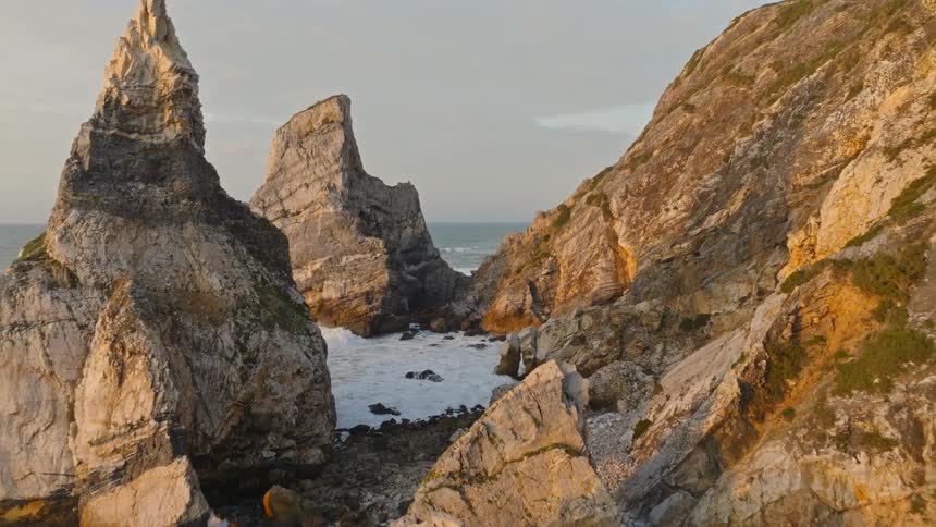 Stunning aerial pullback reveals the epic sea stacks and hidden sands of Praia da Ursa beach in Portugal at golden hour
