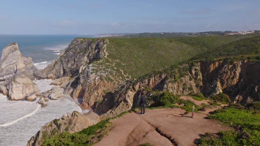 A man and a child stand on a dramatic cliffside enjoying the panoramic view of the rugged coastline and the ocean below