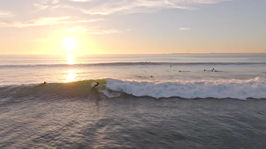 An epic aerial slow-motion shot of a surfer skillfully riding a long, perfect wave during a golden sunset