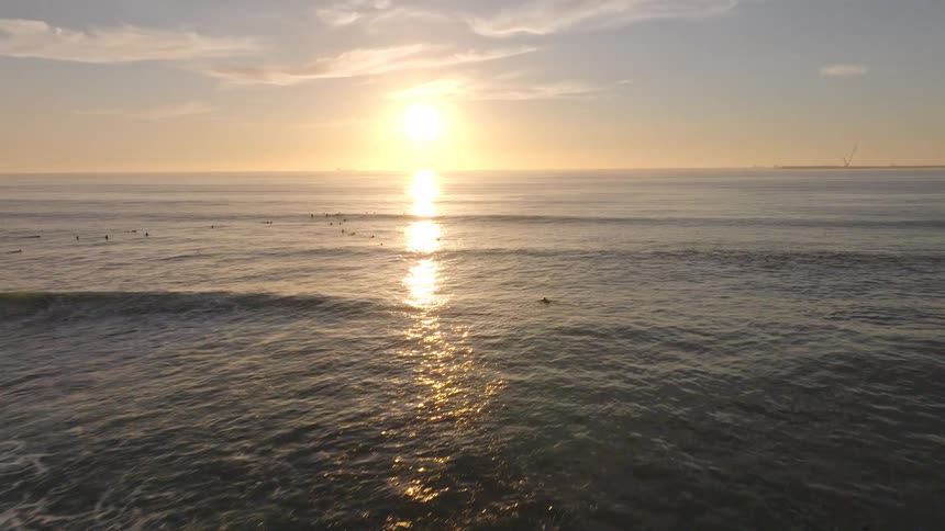 An aerial view of the sun rising over the ocean as surfers wait for the morning waves