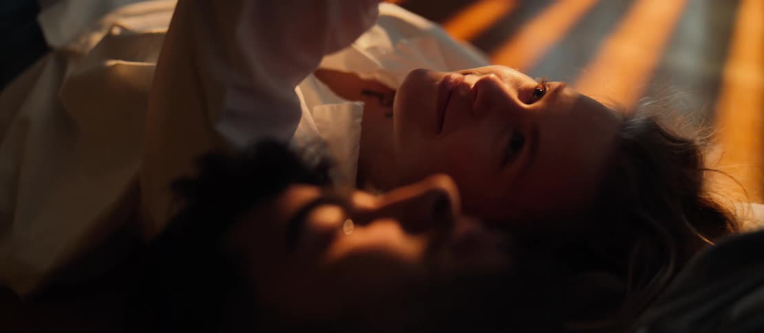 An intimate close-up shows a happy young woman lying beside her partner, both basking in the warm glow of sunlight
