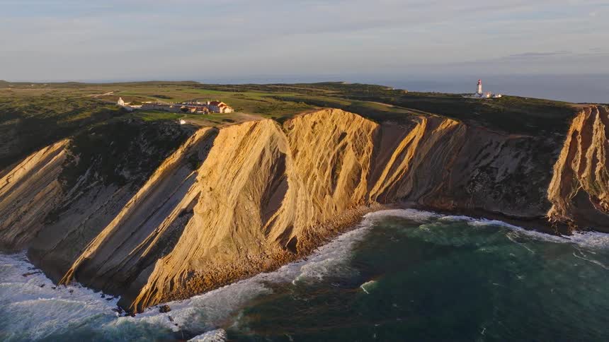 Aerial view of the dramatic layered cliffs and lighthouse of Cabo Espichel, Portugal, beautifully lit by the golden hour sun