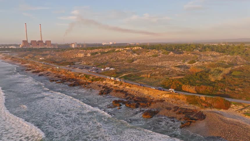Aerial view of a beautiful coastline with a smoking power plant in the background at sunset