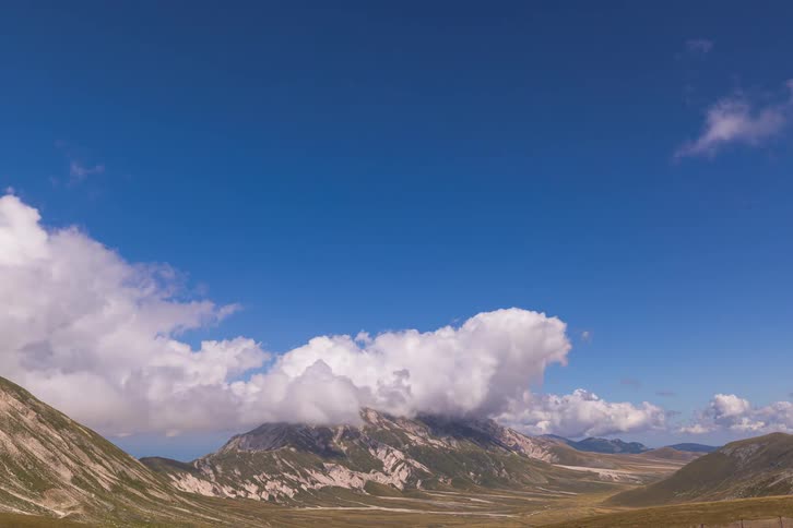 Stunning timelapse of beautiful white clouds swirling and forming around a mountain peak in an expansive valley under a blue sky