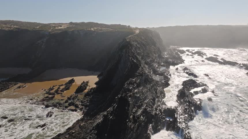 An aerial shot follows a man walking along a precarious cliffside trail before pulling back to reveal the breathtaking coastal landscape and crashing waves