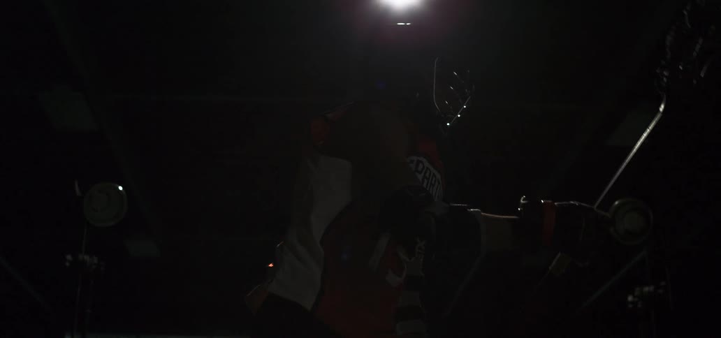 A lacrosse player wearing a helmet and jersey stands in dramatic lighting before a flash reveals his powerful stance in slow motion