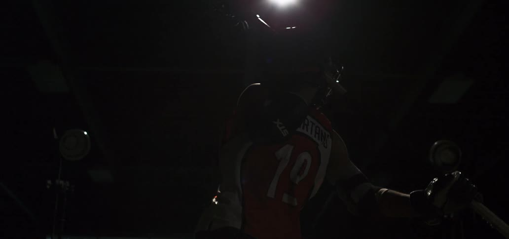 Slow motion shot of a lacrosse player posing with his stick as a bright light flashes in a dark, dramatic setting