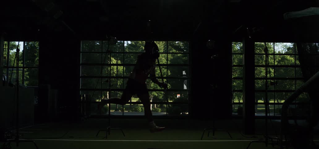 Female lacrosse player leaps through the air to take a powerful shot in a dramatically lit indoor facility in super slow motion