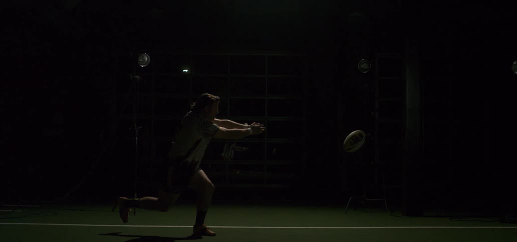 Dramatic slow motion shot of a male rugby player passing a ball in a dark indoor training facility with strobing lights