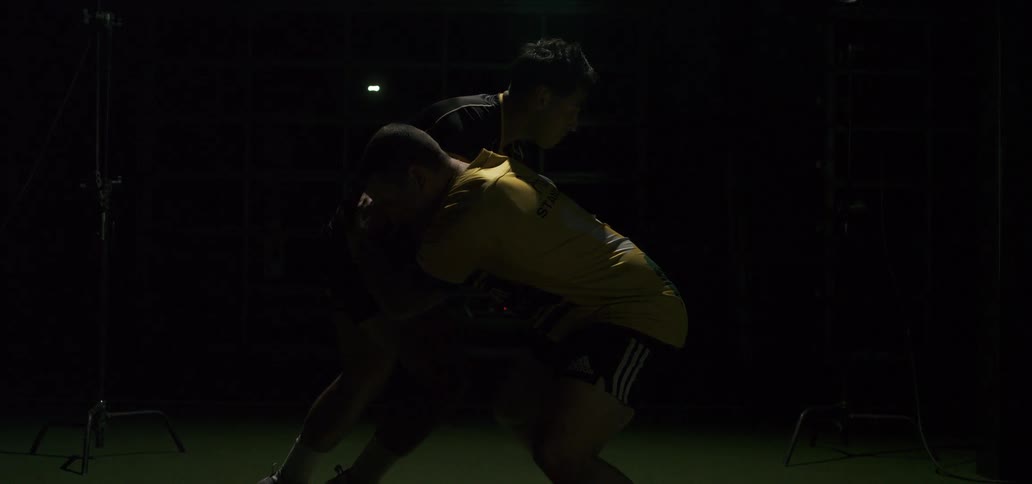 Two muscular rugby players are locked in a scrum position in slow motion with dramatic lighting in a studio