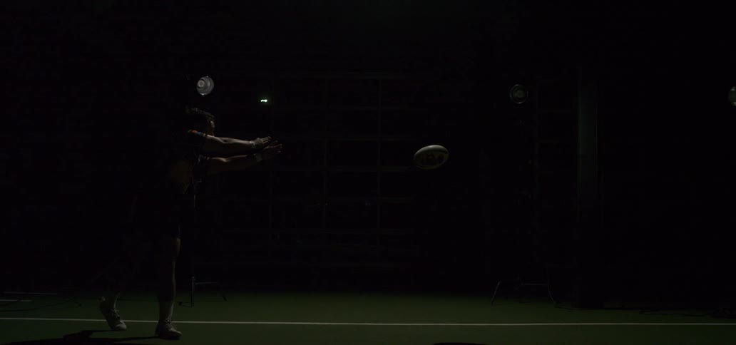 Dramatic slow-motion footage of a rugby player throwing a pass, illuminated by flashing studio lights