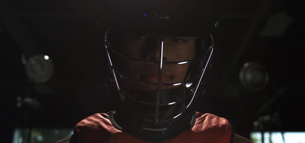 A determined lacrosse player in full gear stares intensely at the camera under dramatic cinematic lighting