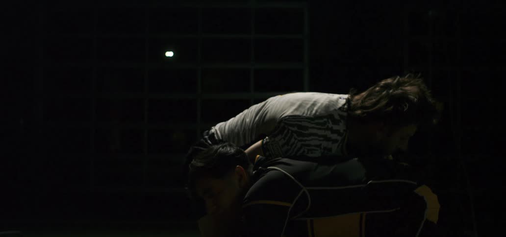 Slow motion of two rugged rugby players in a scrum position at night as a bright light flares and illuminates them
