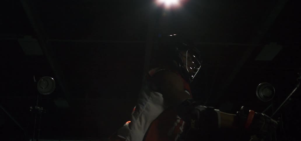 A lacrosse player poses with his stick in slow motion under dramatic studio lighting