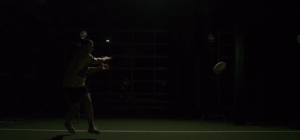 Super slow motion of a rugby player throwing a ball with a strobe light effect in a dark studio