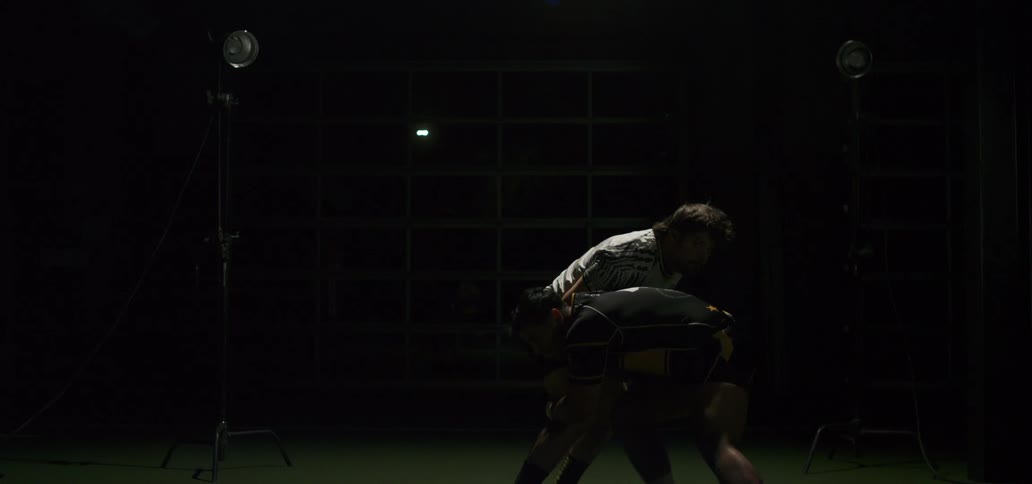 Two rugby players perform a tackle in super slow motion in a dramatically lit studio setting with flashing lights
