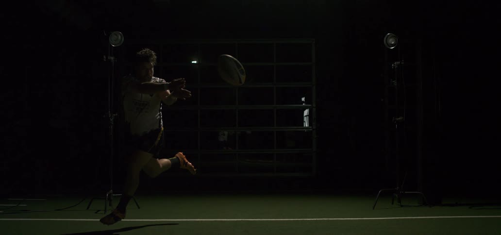 A male rugby player throws a ball in super slow motion as lights flash in a dark studio