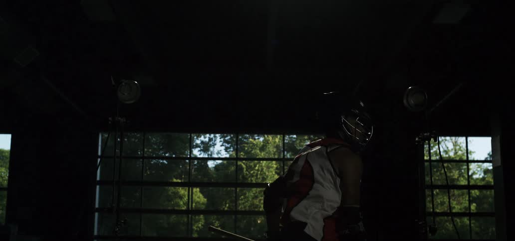 A female lacrosse player in full uniform and helmet cradles the ball on her stick in a dramatically lit studio in slow motion
