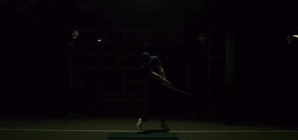 Dramatic slow motion of a man swinging a golf club with a strobe light effect in a dark indoor training facility