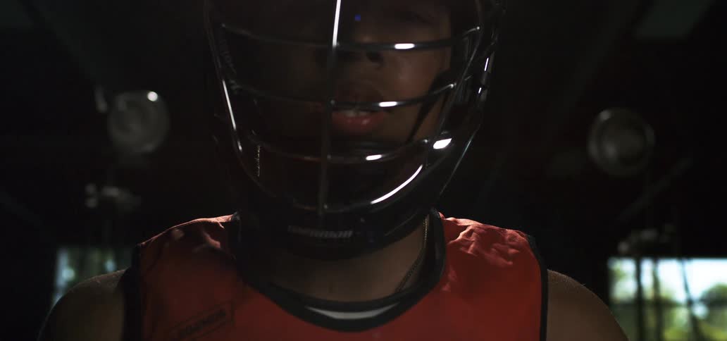 Close up of a focused young lacrosse player in a helmet with dramatic lighting and lens flares