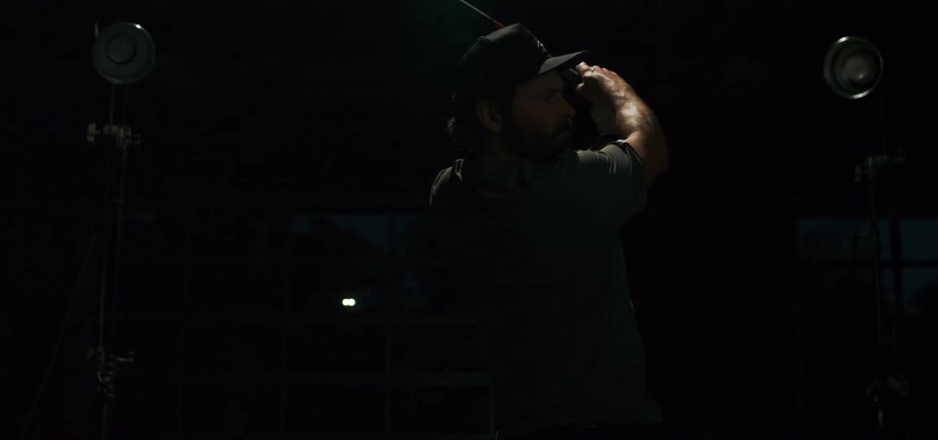 A male golfer swings his club in slow motion, illuminated by a dramatic flashing light in a dark setting