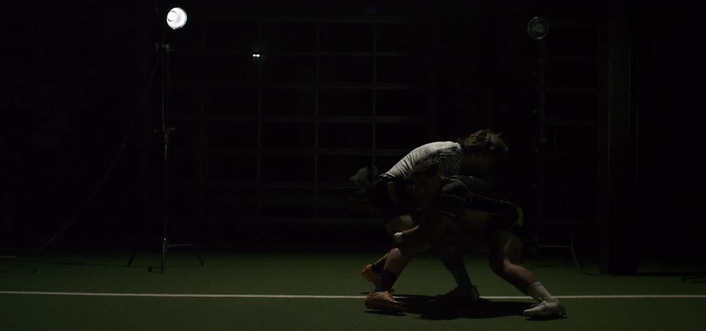 Two muscular male rugby players grapple and tackle in a dramatic, slow-motion sequence under intense studio lighting