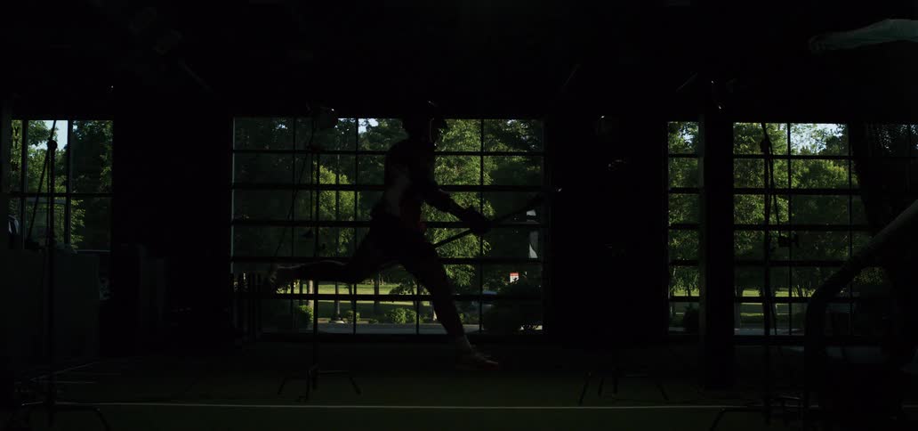 A lacrosse player is dramatically lit by a strobe flash while shooting and running in slow motion inside a training facility