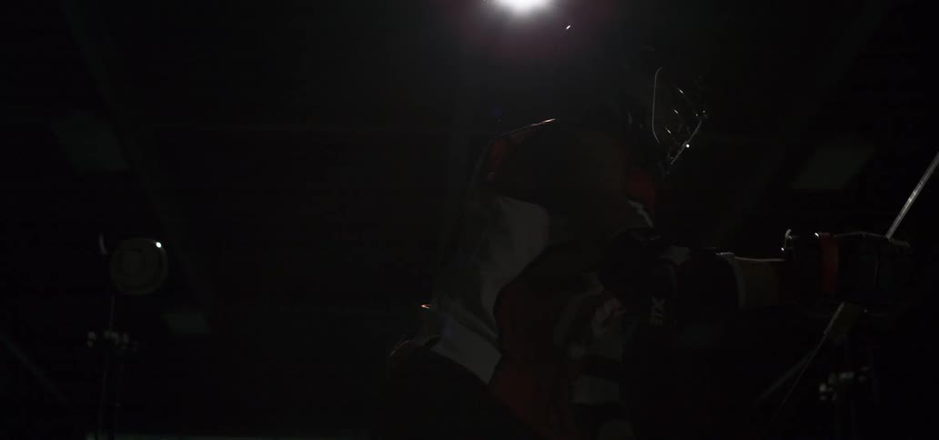 A dramatic, slow-motion shot of a lacrosse player posing with his stick under a spotlight before walking away