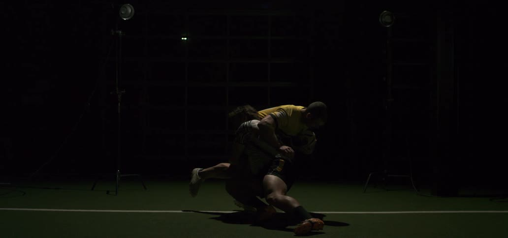 A rugby player tackles an opponent to the ground in a dramatic slow motion shot under studio lights