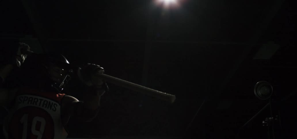 Dramatic slow-motion pan of a lacrosse player in a dark room following through on a powerful shot