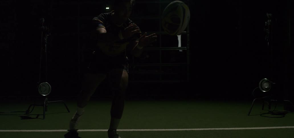 A male rugby player passes a ball in super slow motion with dramatic strobe lighting in a studio