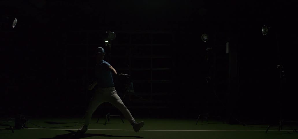 Dramatic slow motion of a baseball pitcher throwing a fastball, highlighted by powerful strobe lights in a dark training facility