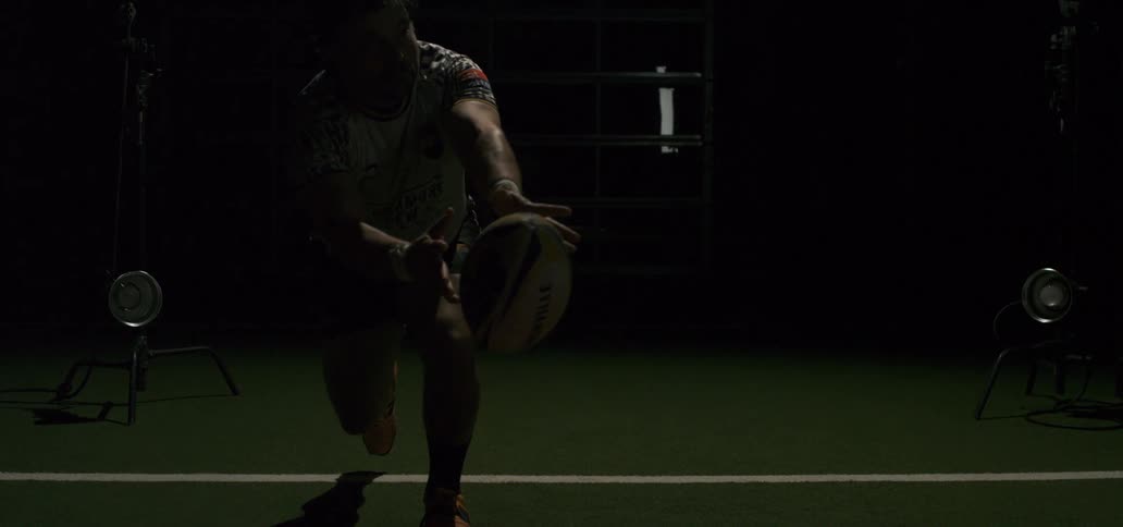 Slow motion shot of a rugby player kicking a ball off a tee with a dramatic flash of light upon impact