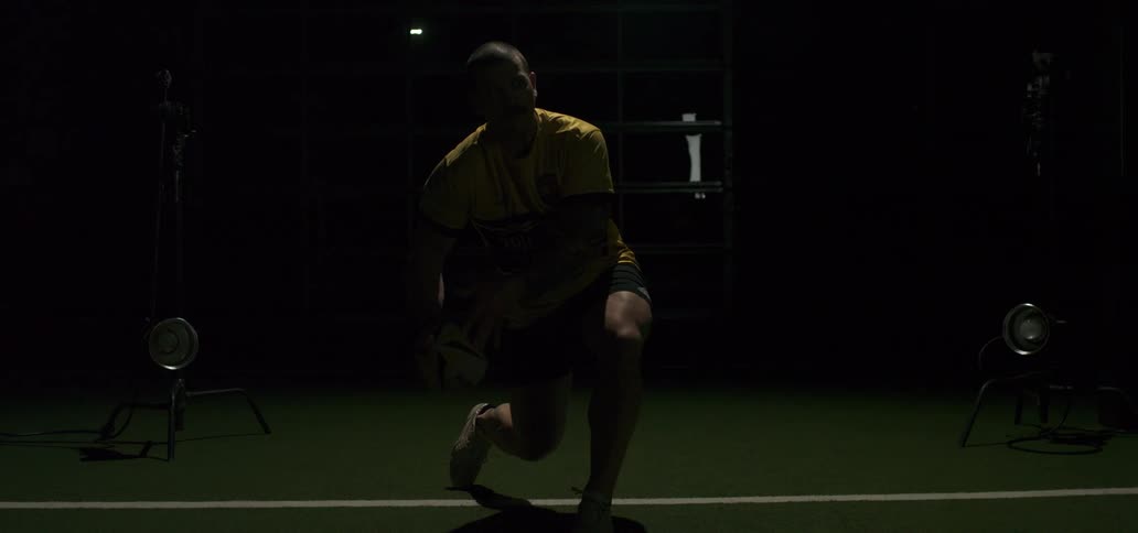 A male rugby player in a dark studio setting passes the ball in dramatic slow motion with bright flashing lights