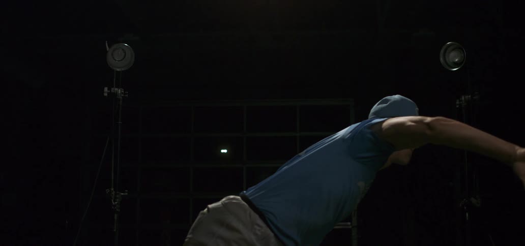 A baseball player throws a pitch in a dark studio in dramatic slow motion with a bright lens flare